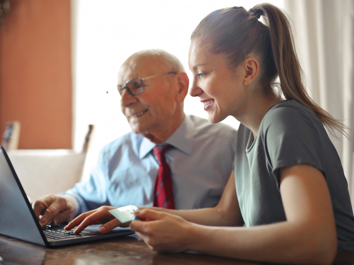 assistance a young woman is assisting an elderly gentleman to make a payment on a laptop
