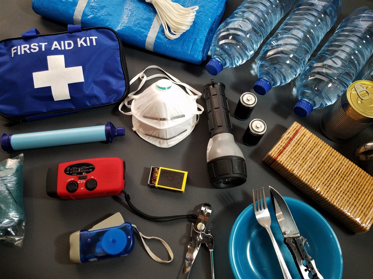 emergency preparedness items such as bottled water, a first aid kit, a flashlight and canned goods are displayed on a gray background.