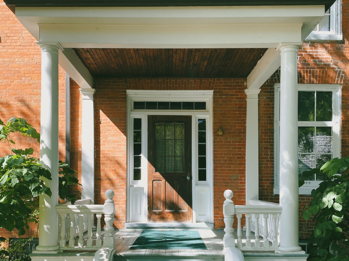 an older orange brick home with a white porch, gray steps and a dark brown wooden door