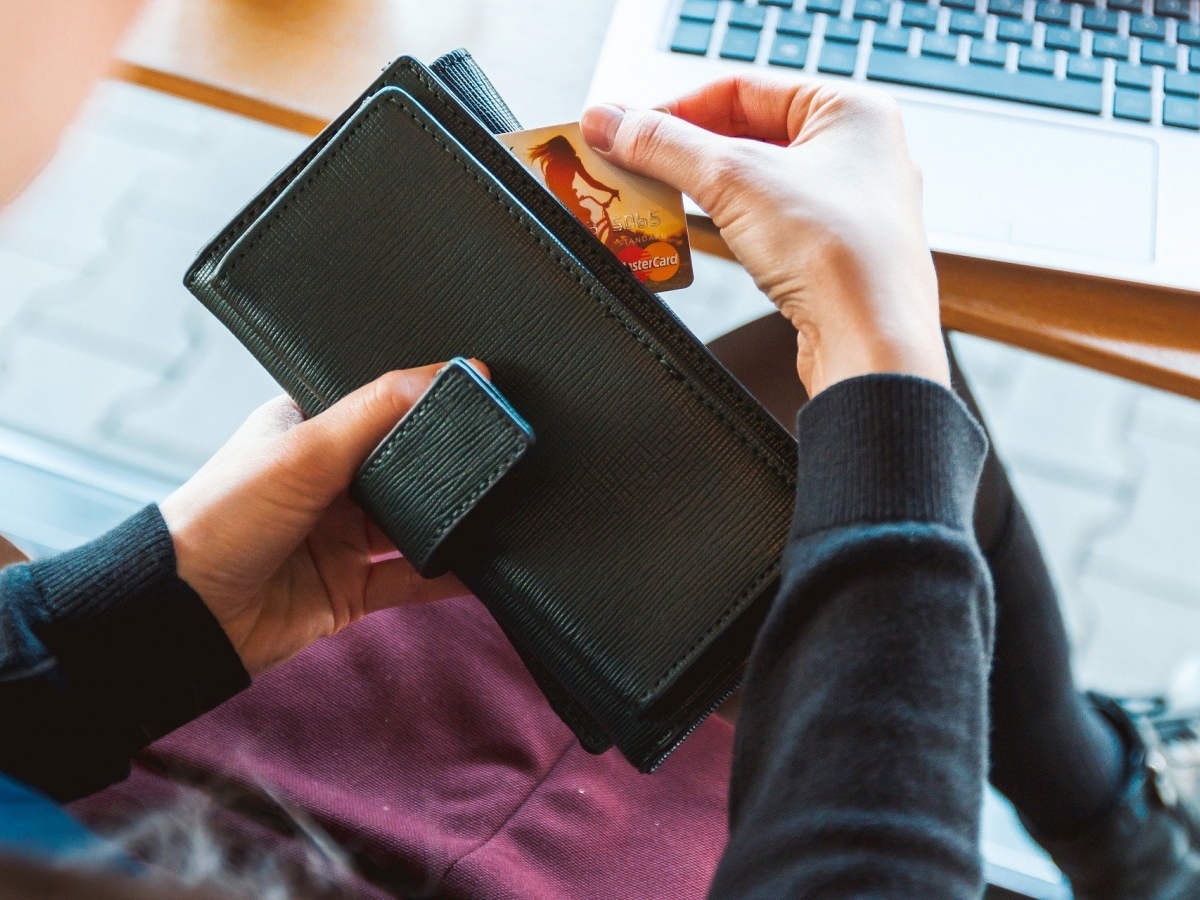 Picture of a person's hands holding a black wallet with a mastercard partially removed